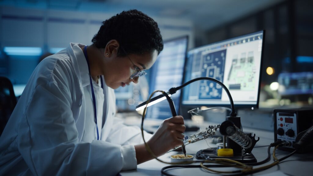 Modern Electronics Research, Development Facility: Black Female Engineer Does Computer Motherboard Soldering. The image is representative of the upcoming fellowship deadline for the NASA Postdoctoral Program.
